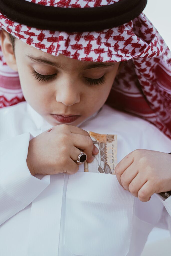 pexels-photo-21553490-21553490 Portrait of a Cute Boy in a Traditional Headscarf and Wear Putting a Banknote in a Pocket of his Shirt